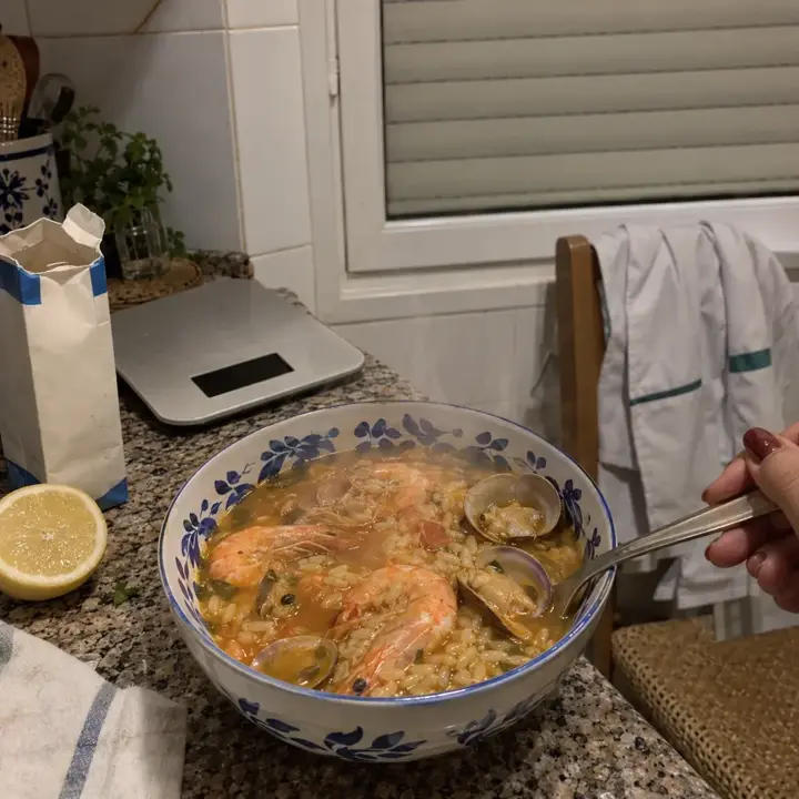 Cuenco de arroz caldoso de marisco con gambas y almejas en una cocina pequeña de noche