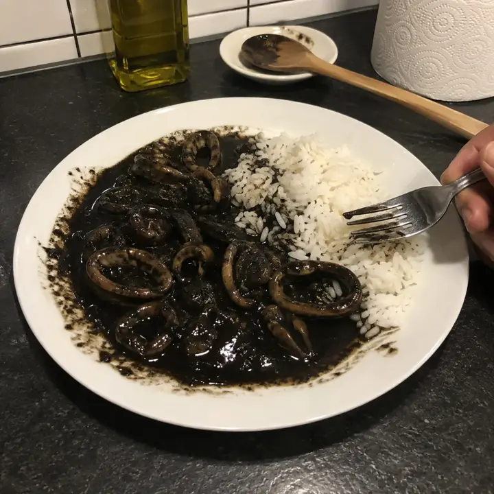 Plato de calamares en su tinta con arroz blanco en la encimera de una cocina por la noche