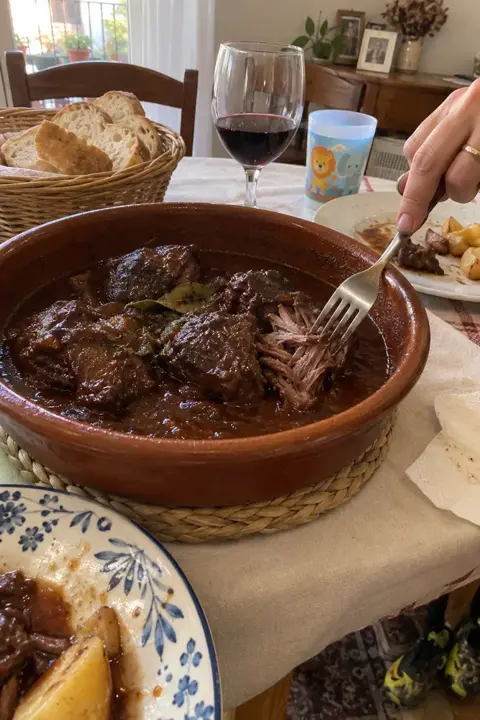 Cazuela de barro con carrilleras en salsa de vino tinto sobre la mesa de un domingo