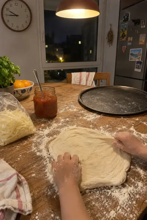 Manos de niños estirando masa de pizza en una mesa de madera llena de harina